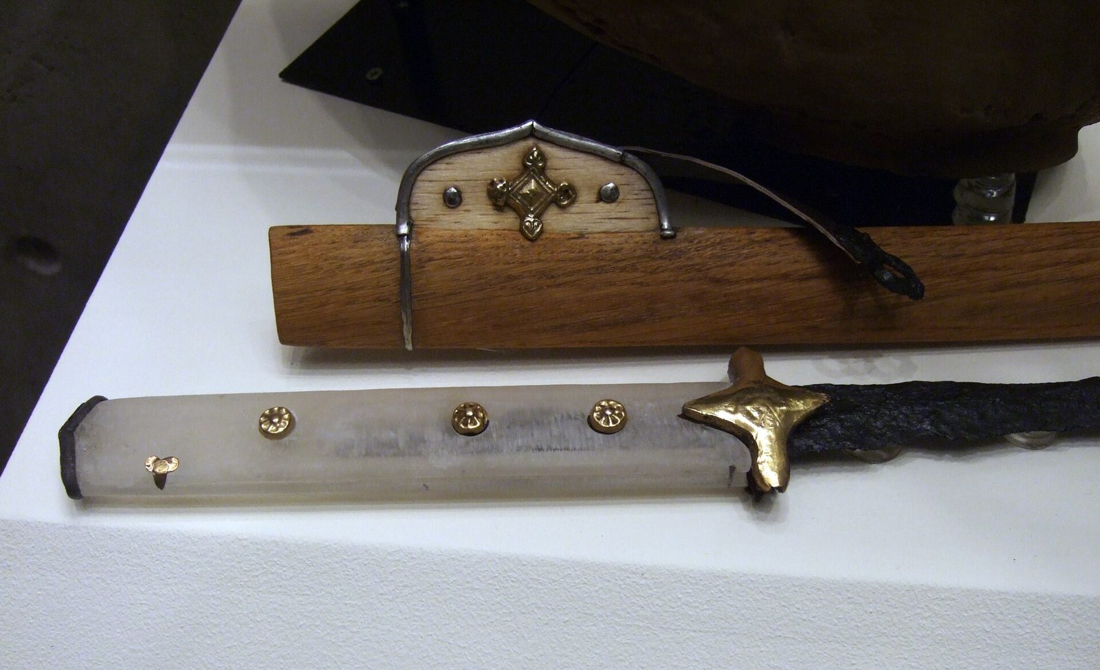 A curved iron sabre with gilt mounts lying beside its wooden sheath in a museum case.