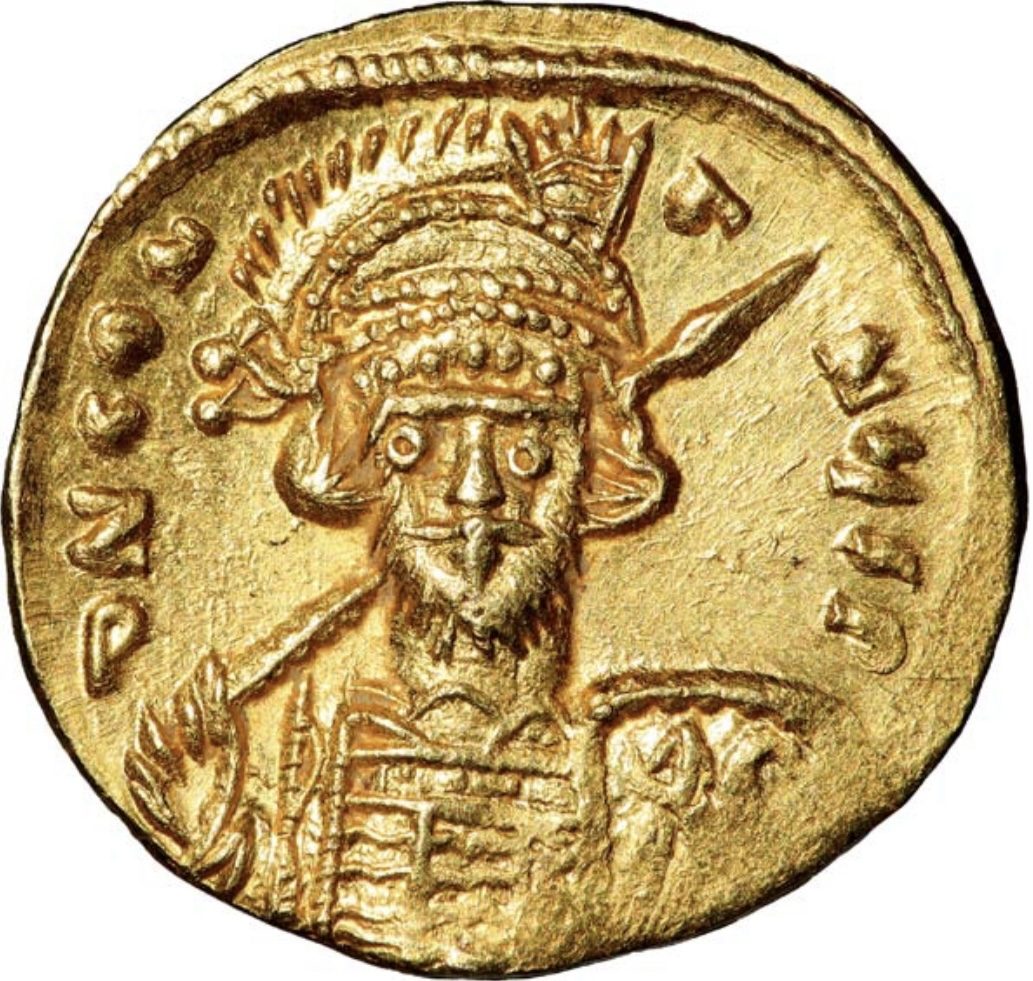 A gold coin showing a bearded emperor facing forward in a plumed helmet, holding a spear over his shoulder.