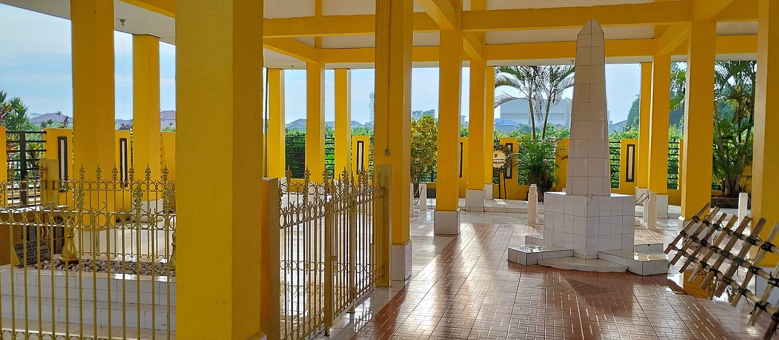 A white grave monument inside a yellow-pillared open pavilion behind railings.