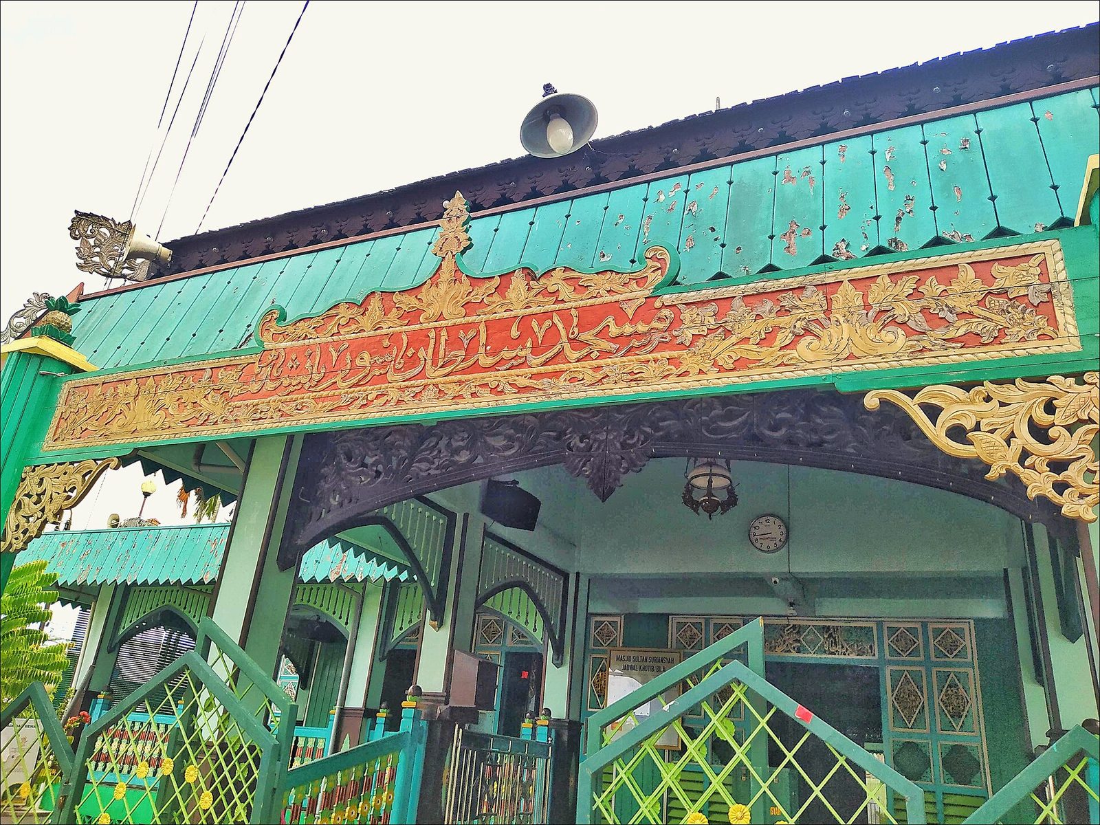 A green and white timber mosque front with carved and painted panels over a wide entrance.