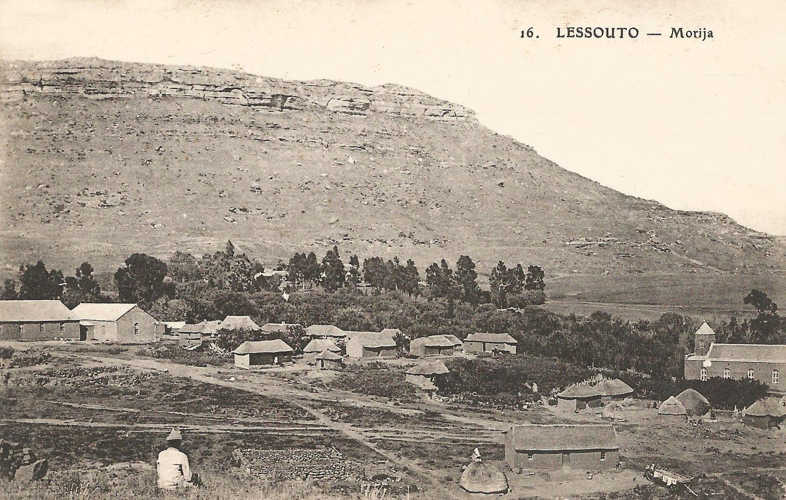 An old photograph of a scatter of mission buildings and houses under a long flat-topped mountain.