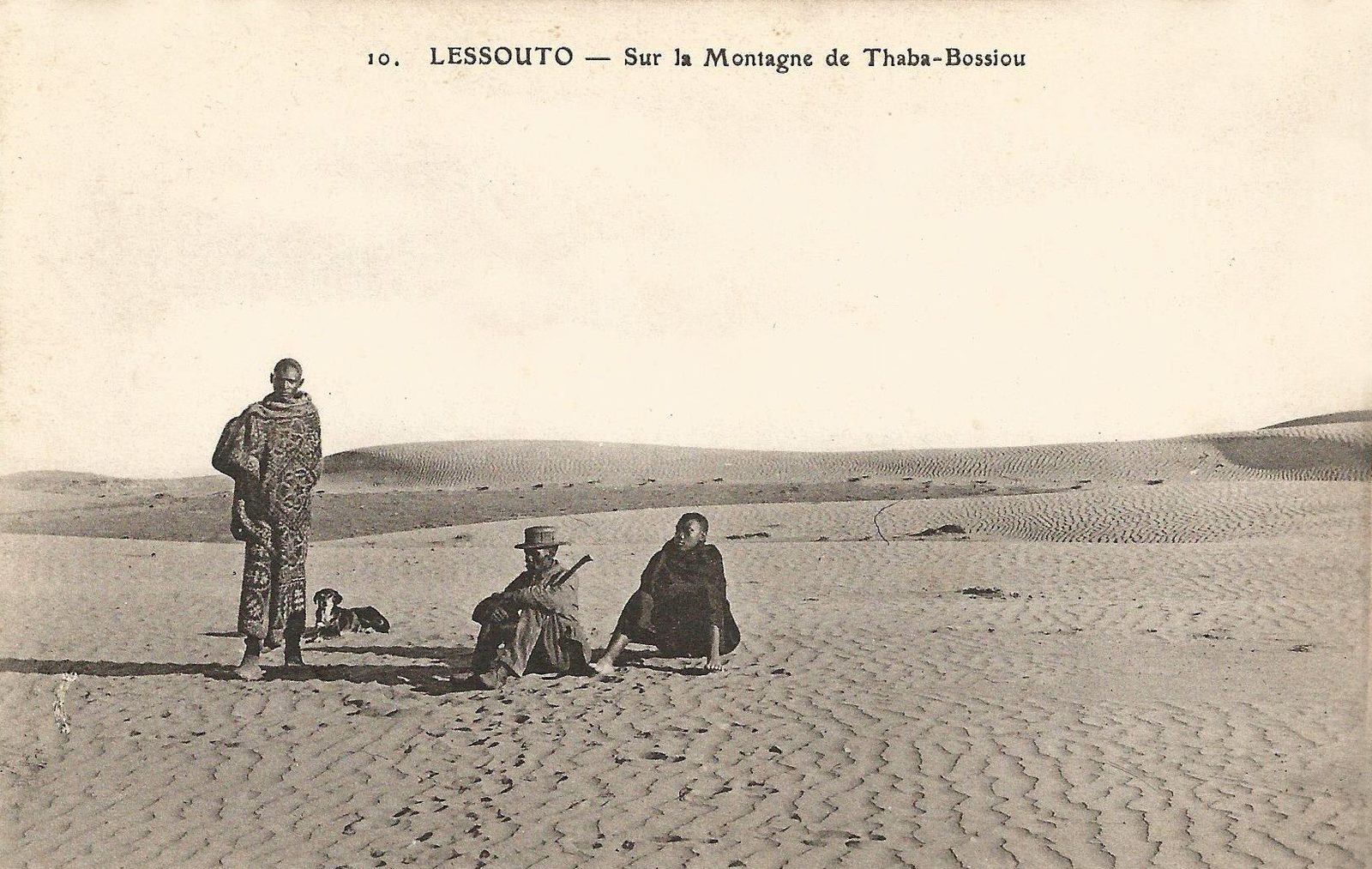 An old photograph of three men in blankets on a flat, bare summit, the land falling away beyond.