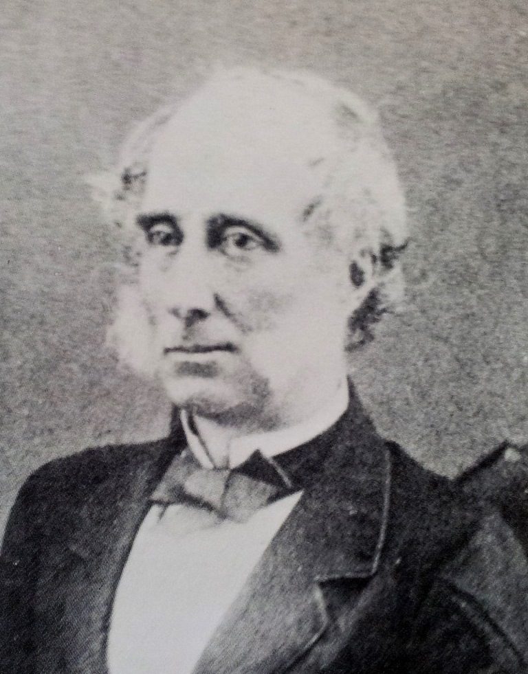 A black-and-white photograph of an elderly man with white side-whiskers and a high collar.
