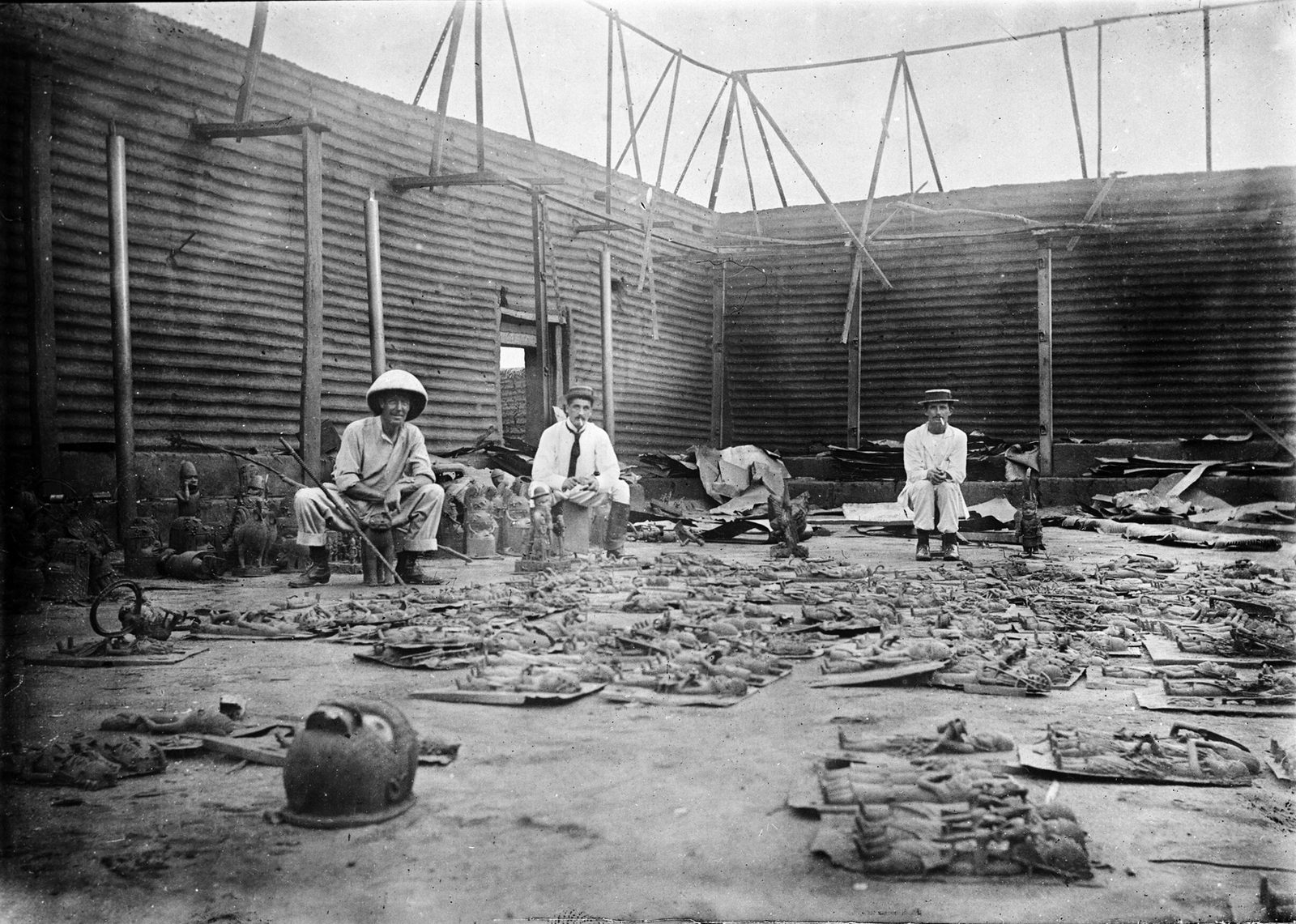 An old photograph of three British officers seated in a roofless burnt courtyard, the floor in front of them covered with brass plaques.