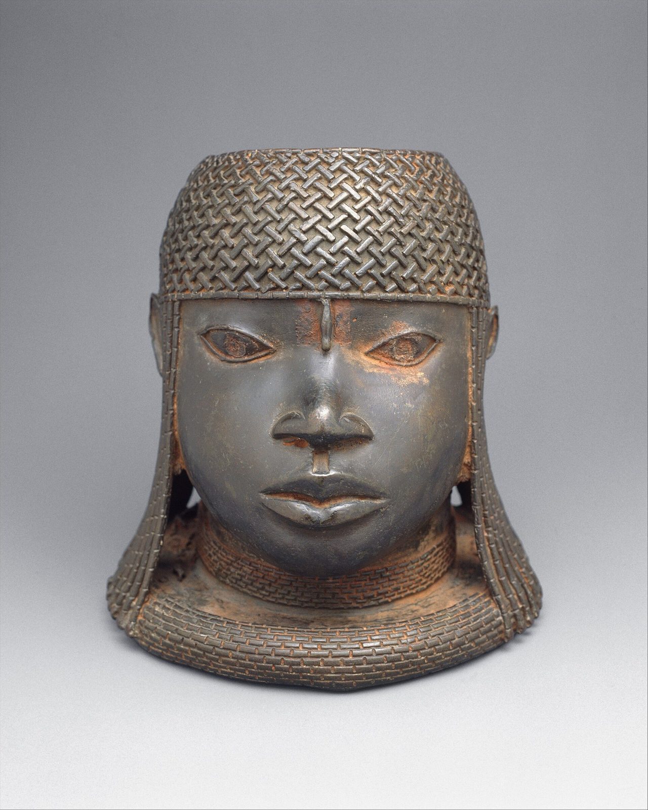 A cast brass head of a king wearing a tall beaded crown and a high beaded collar up to the lips.