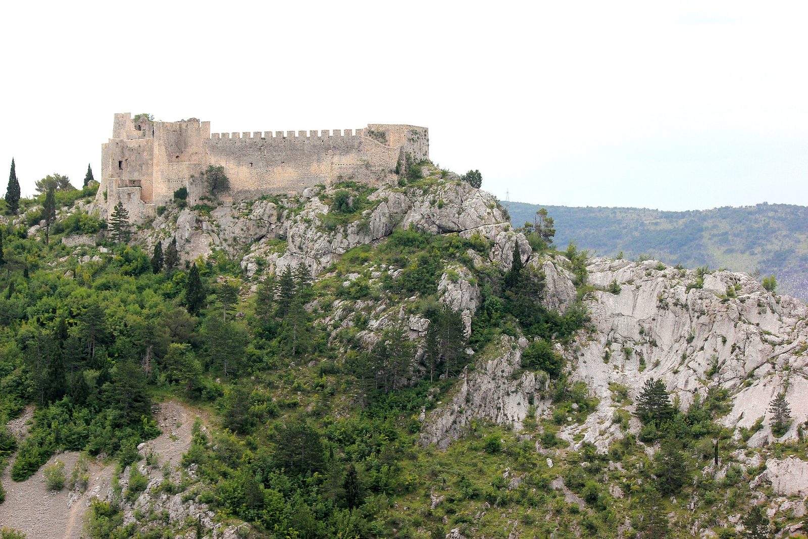 A ruined stone fortress on top of a rocky, wooded crag.