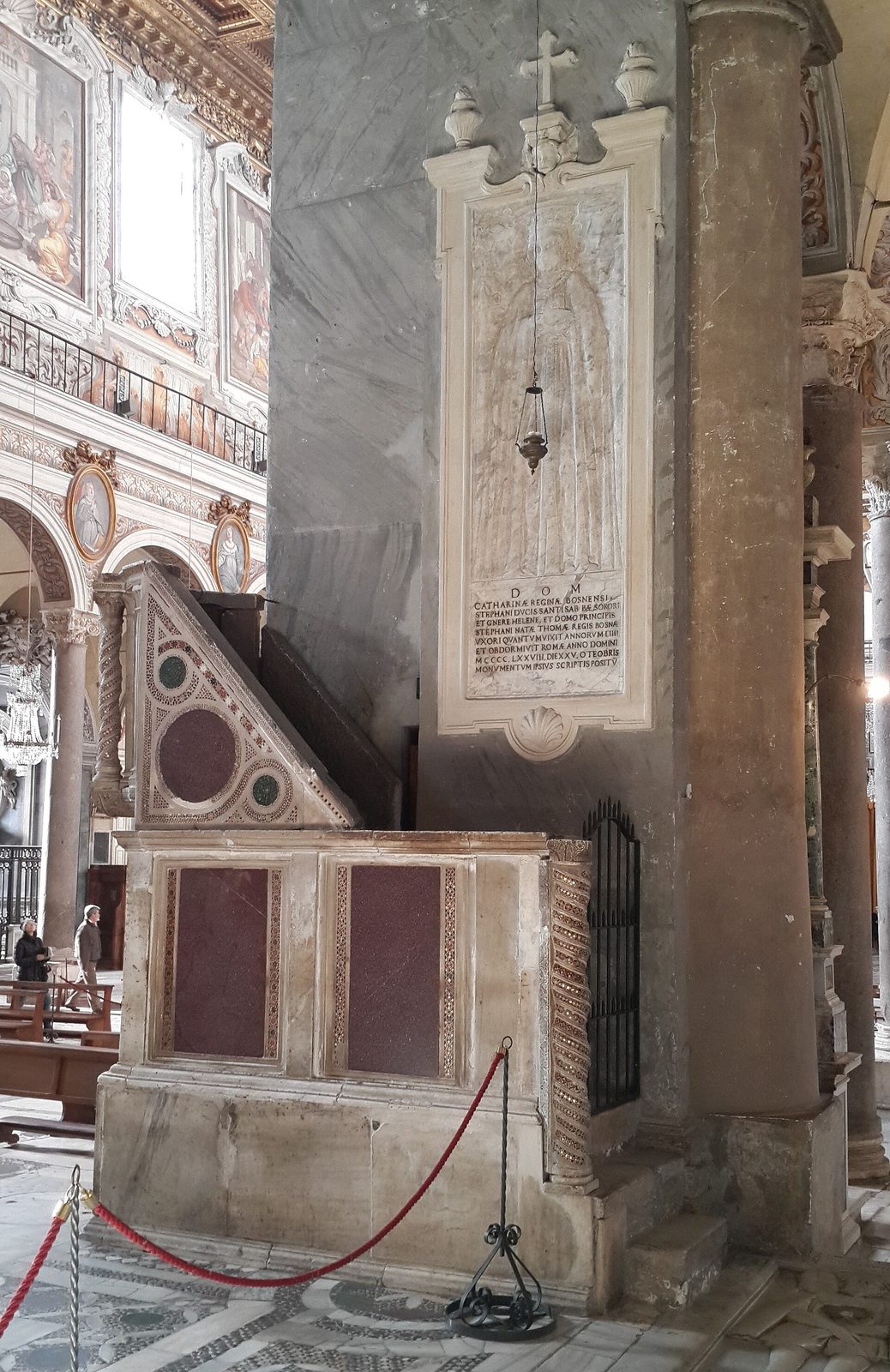 A carved marble tomb slab set upright against a column in a church nave, above a low stone base.