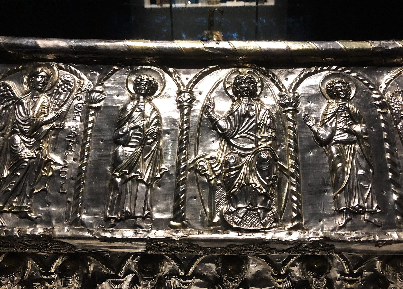 A panel of worked metal in relief, the surface gilded and set with stones, showing figures under an arcade.