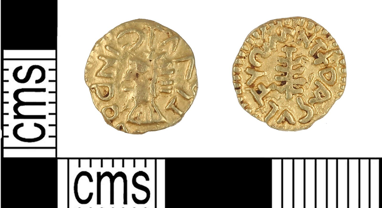 The two faces of a small thin gold coin photographed beside a scale, a crude facing bust on one side and a cross on steps on the other.