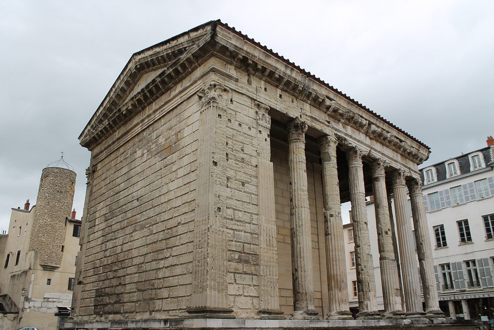 The same temple from another angle, its side colonnade engaged in a plain wall, with a street and parked cars in front of it.