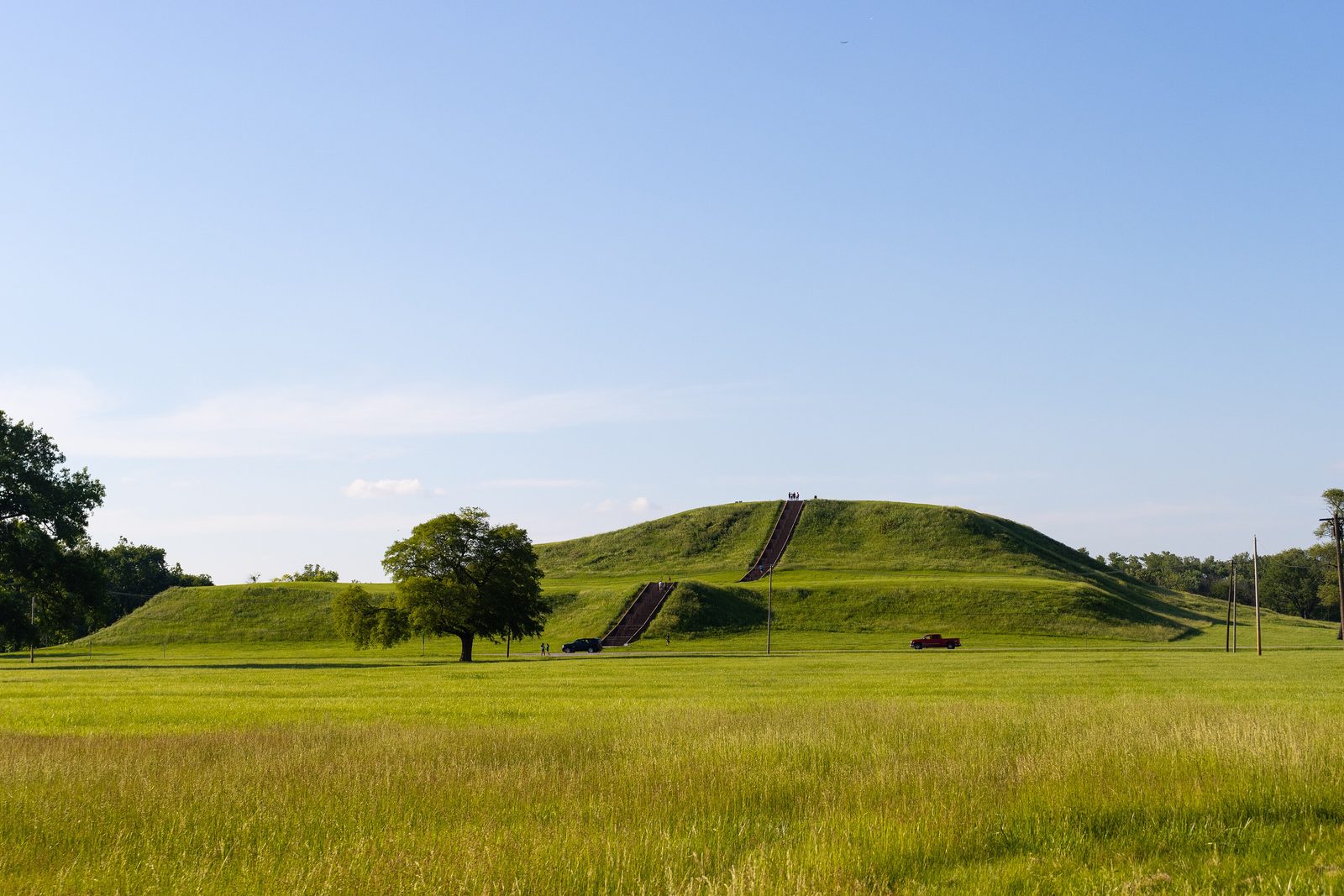A huge flat-topped grass-covered mound with a long staircase up its face, seen across a meadow.