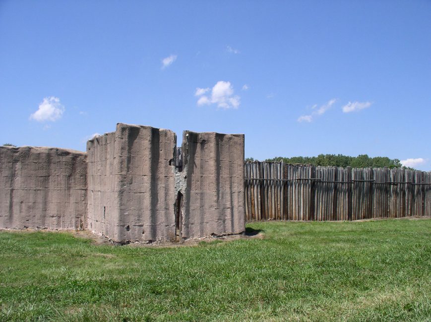 A reconstructed wall of tall upright logs with a projecting square bastion.
