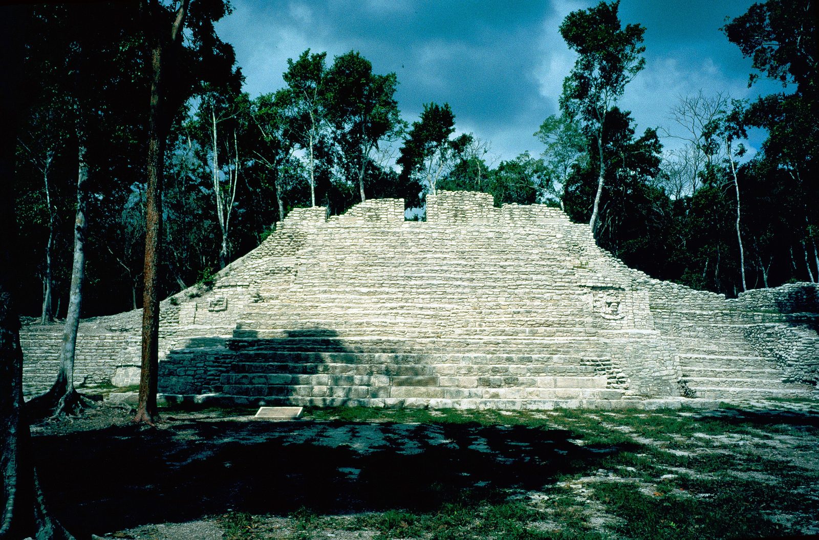 A broad stepped stone building in a forest clearing.