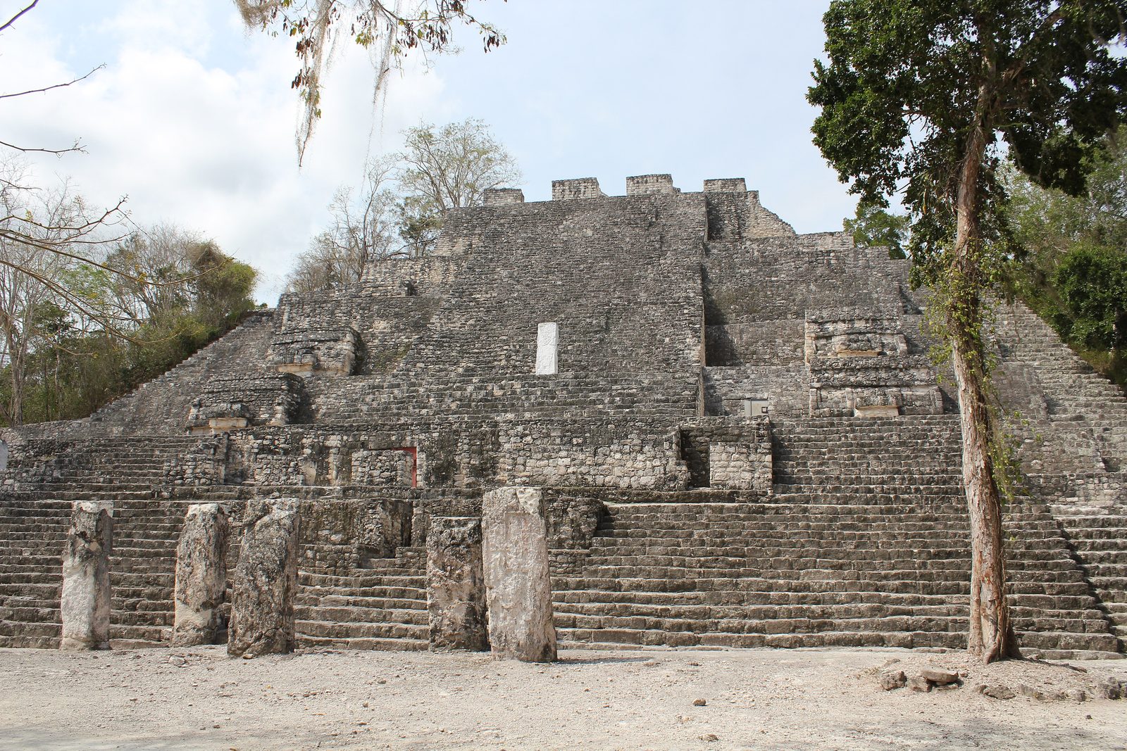 A massive stepped stone pyramid with stelae standing at its base.