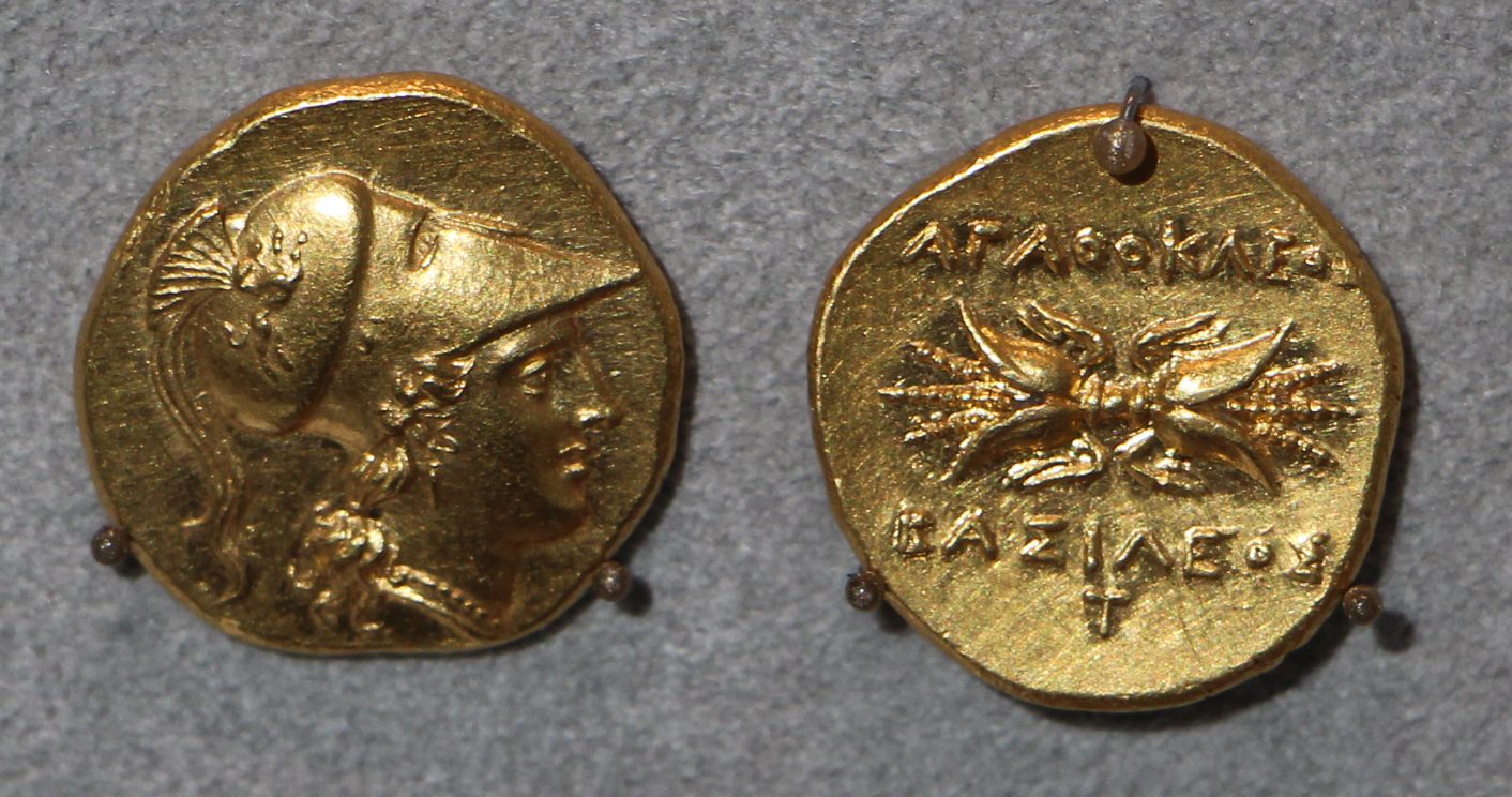 Both faces of a small gold coin: a helmeted head, and a thunderbolt with a Greek legend.