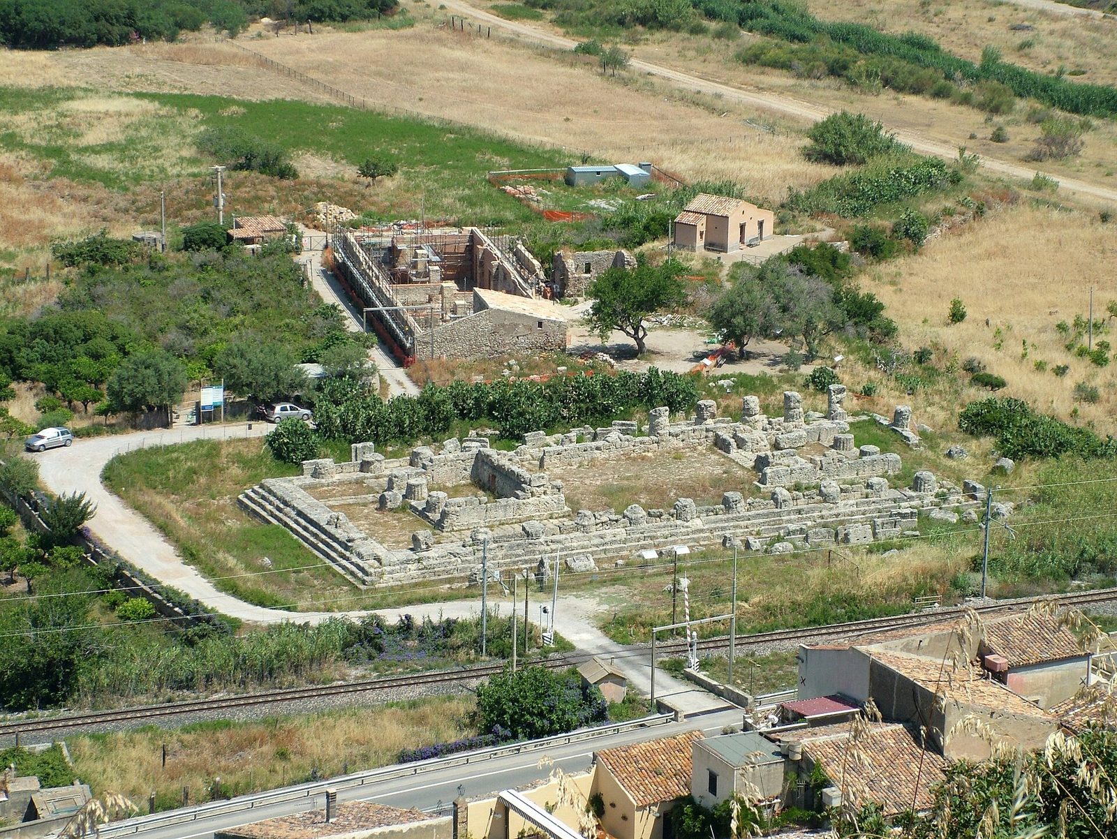 An aerial view of the stone foundations of a large rectangular temple among fields and roads.