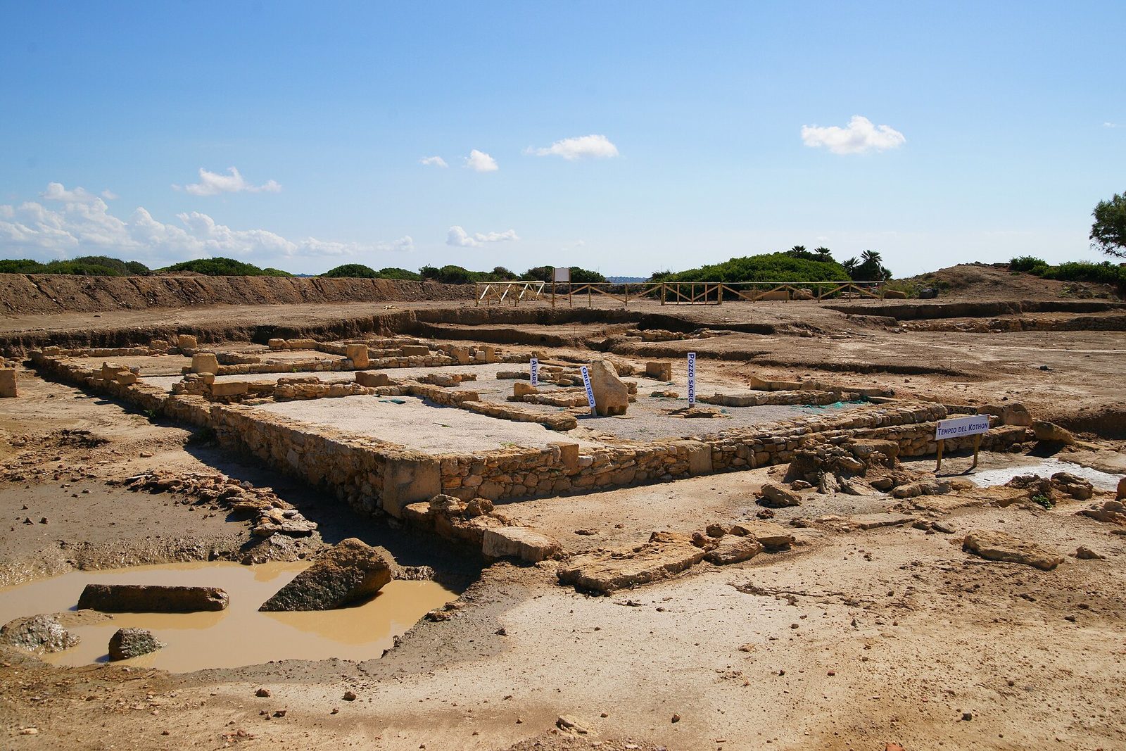 Excavated stone foundations of a rectangular enclosure around a shallow pool on a flat island.