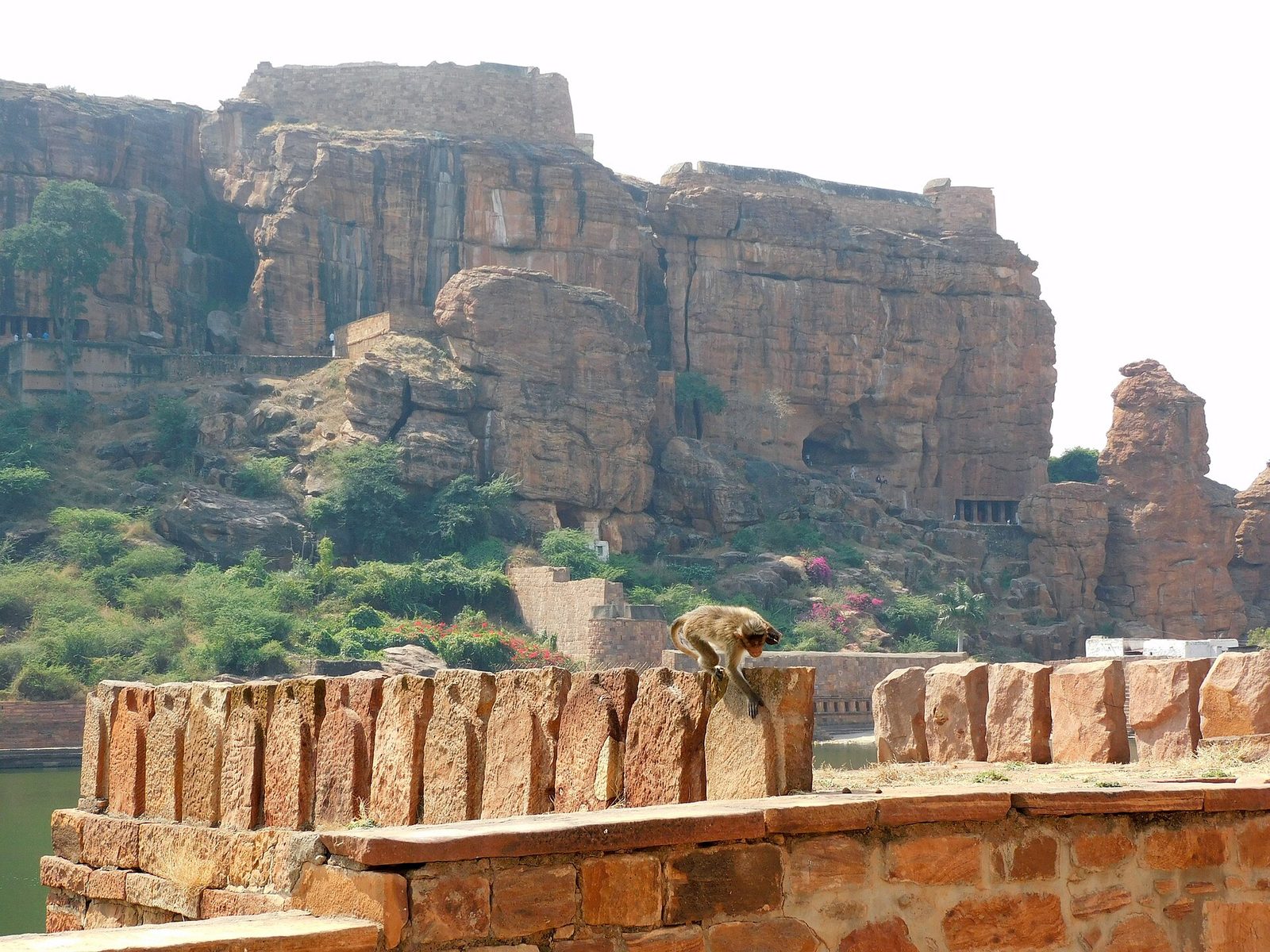 Red sandstone cliffs with rock-cut caves above a lake and its stone steps.