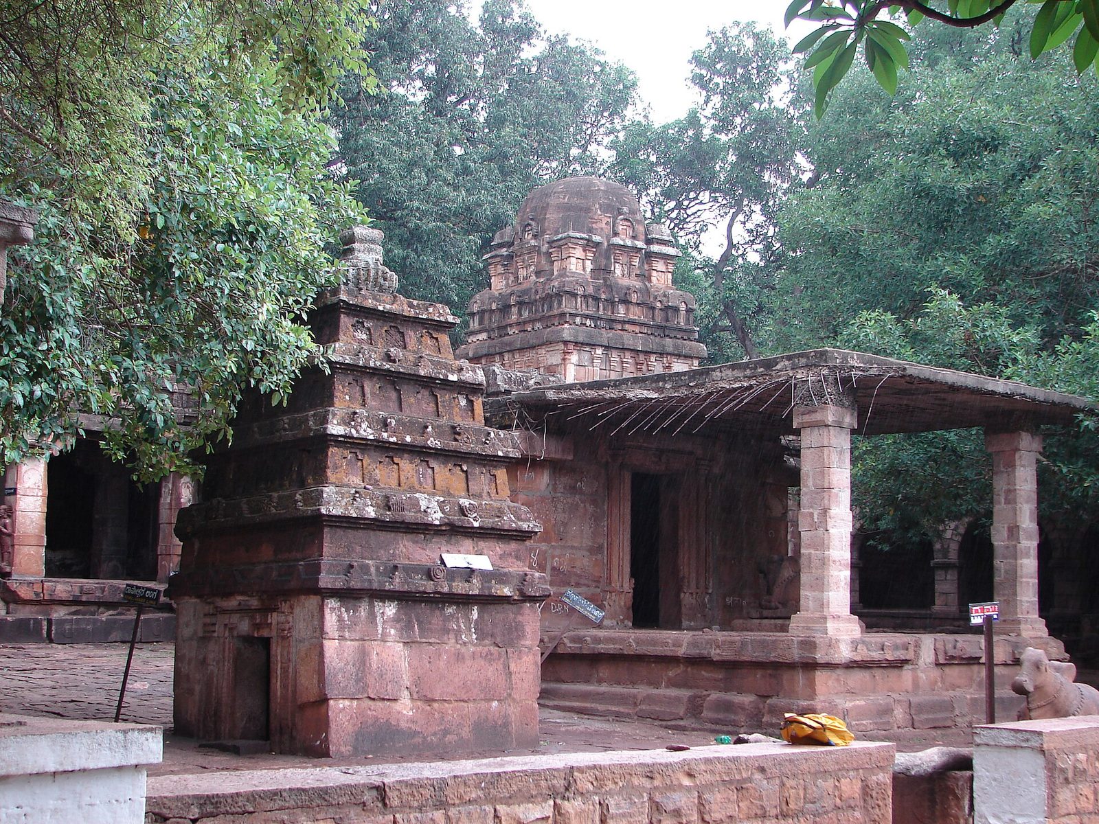 A small stone temple with a stepped tower beside a pillared porch among trees.