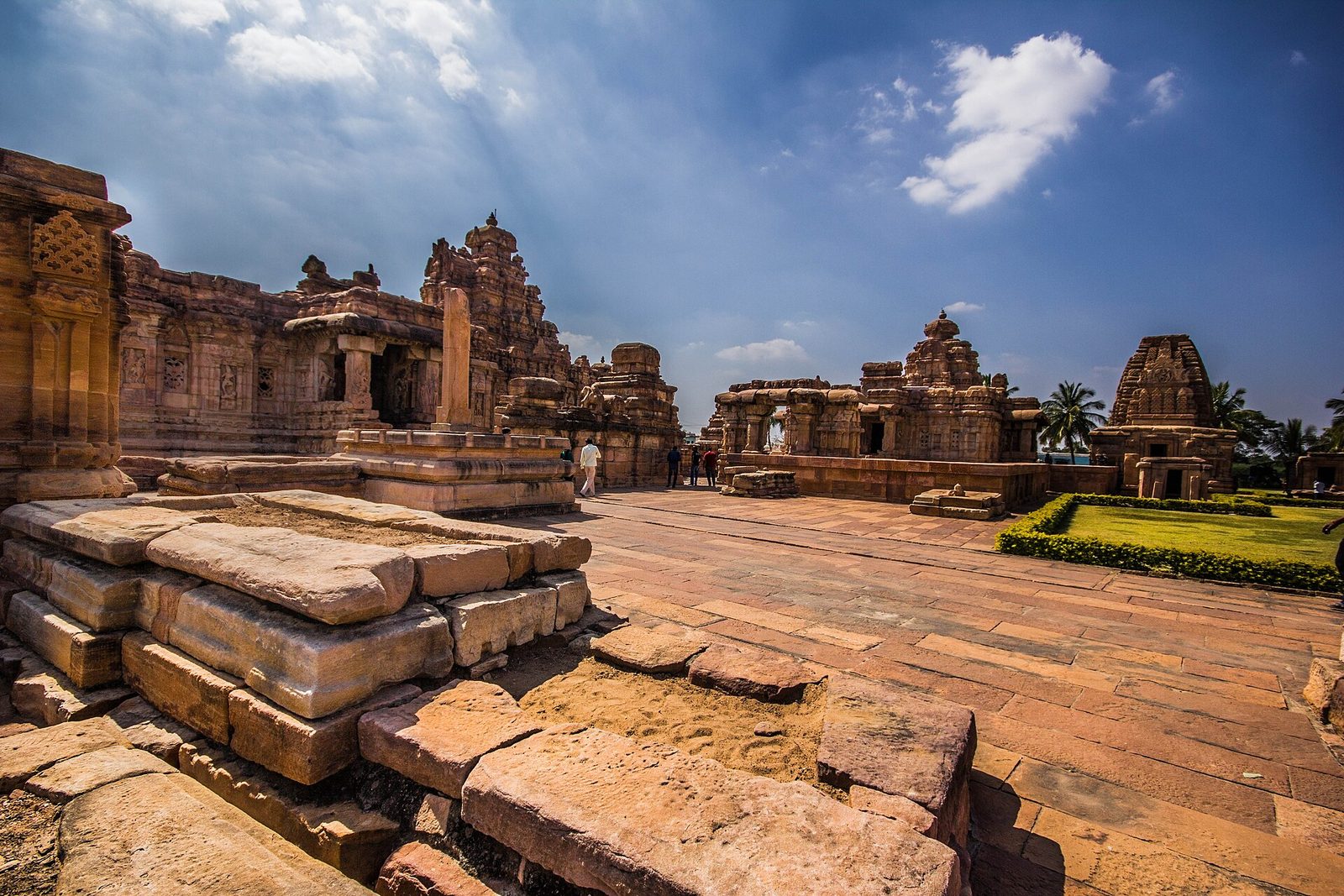 A broad sandstone temple with a pyramidal tower, with a victory pillar in the foreground.