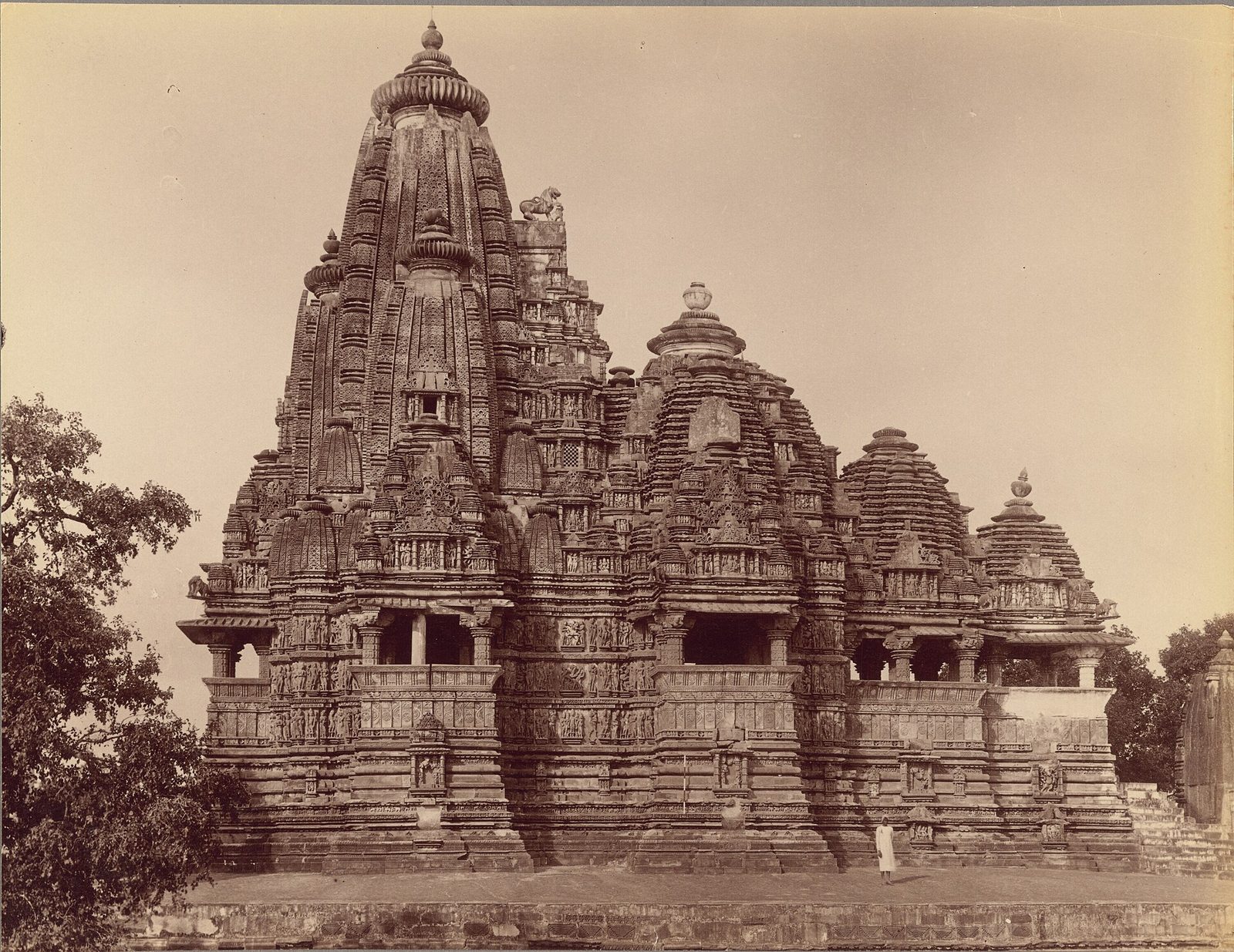 An old photograph of a large temple with rising clustered spires, a man standing before it.