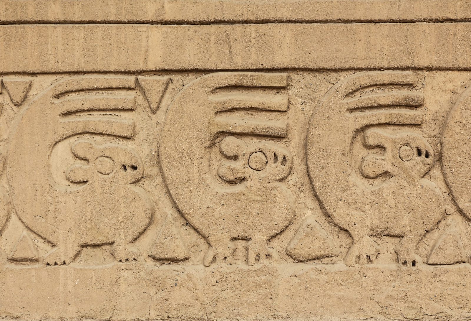 A frieze of stylized squirrel-like animals carved in relief on a clay wall.