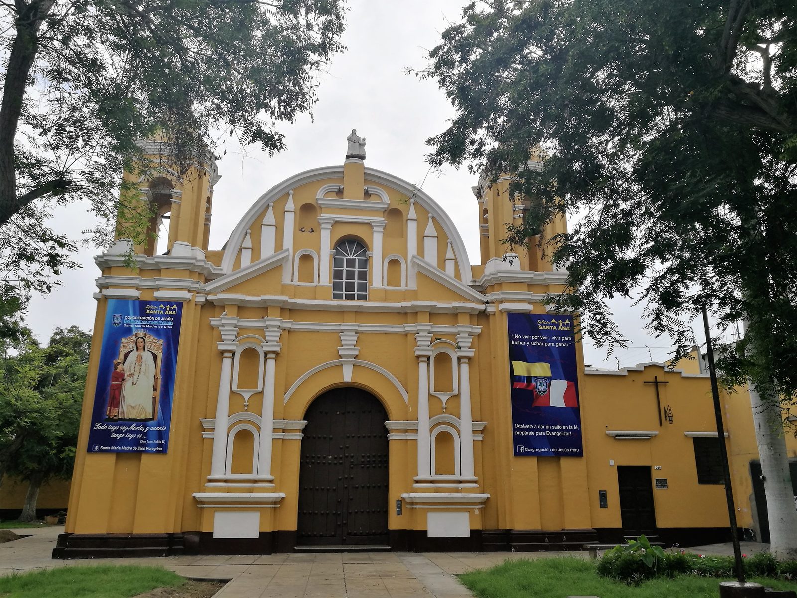 A yellow and white church front with twin towers and banners.