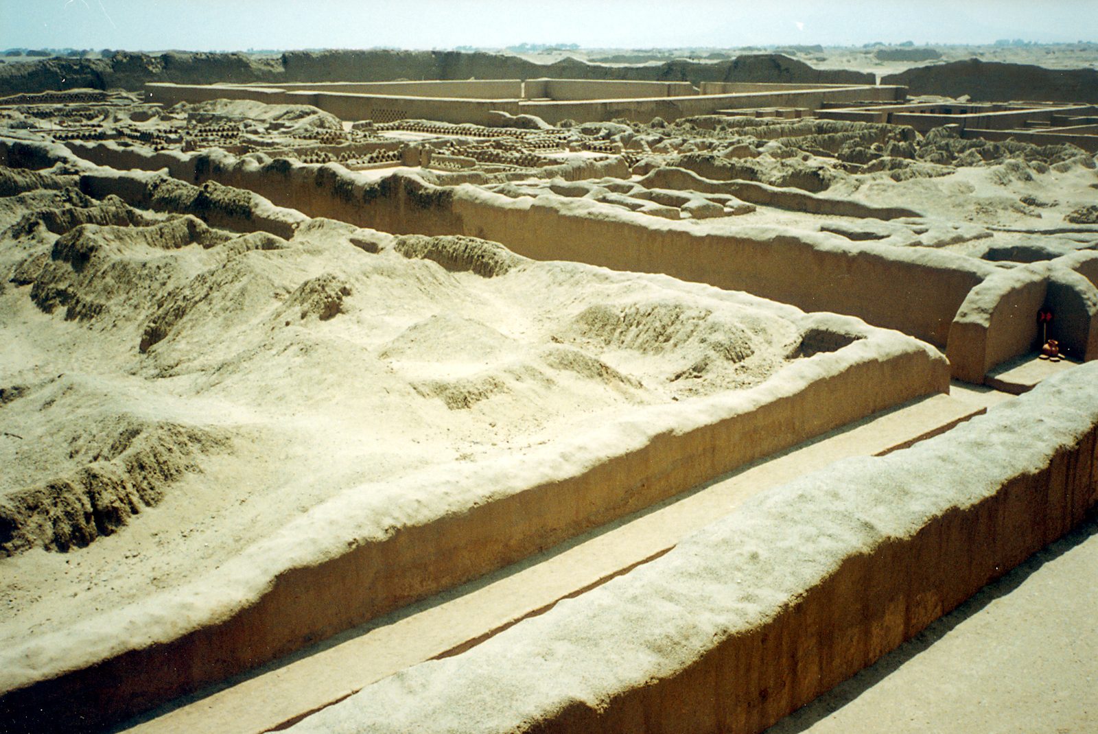 Long eroded adobe walls enclosing courts and passages across a sandy plain.
