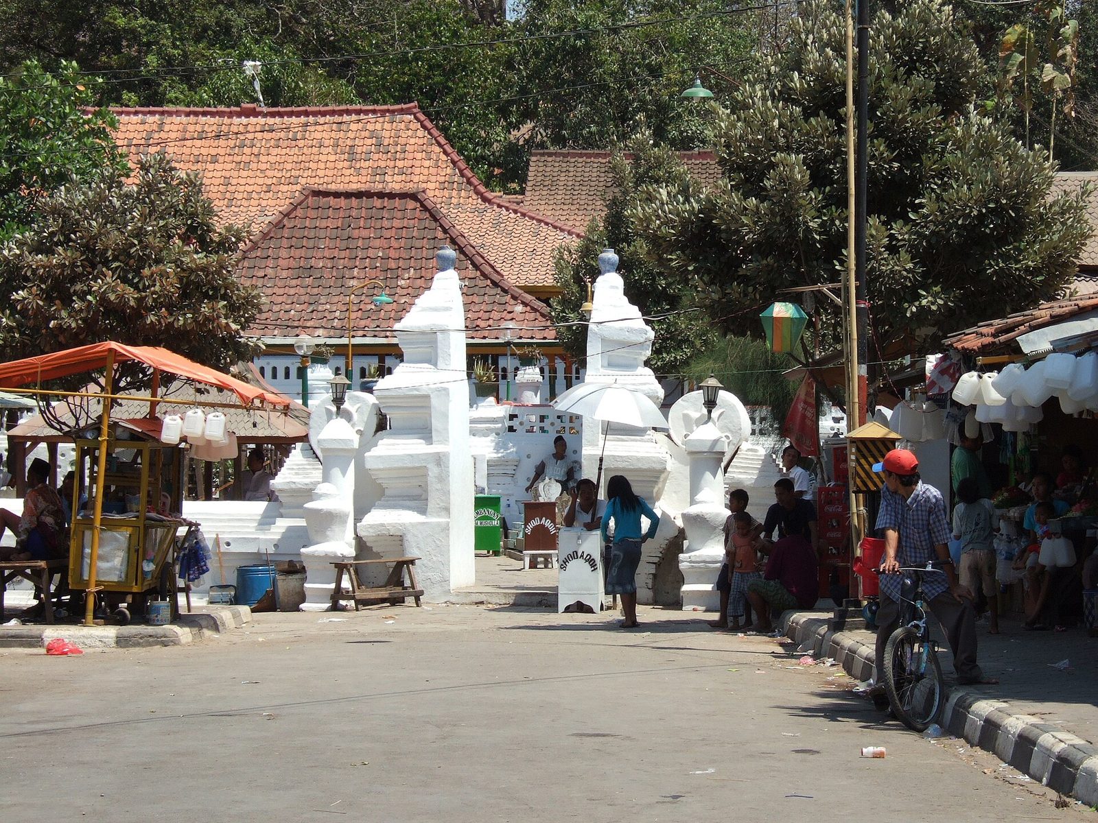 A busy approach to a shrine: white split gateways and walls, food stalls and pilgrims along the road in front.