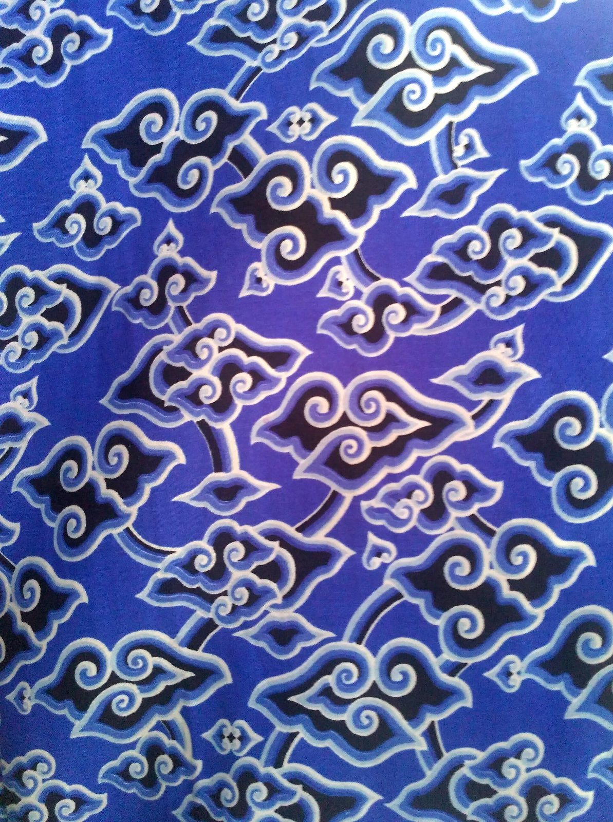 A batik cloth printed with stylised clouds in blue and white, each cloud outlined in graded bands of shading.