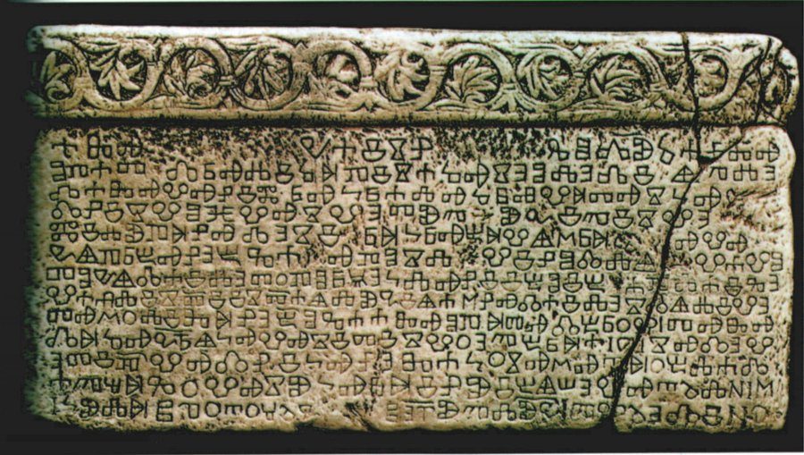 A long stone slab carved with lines of Glagolitic letters under a band of scrolling vine ornament.