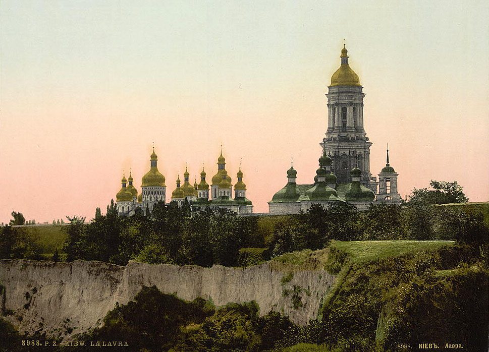 A colour photochrom of gilded church domes and a tall bell tower on a wooded hill.