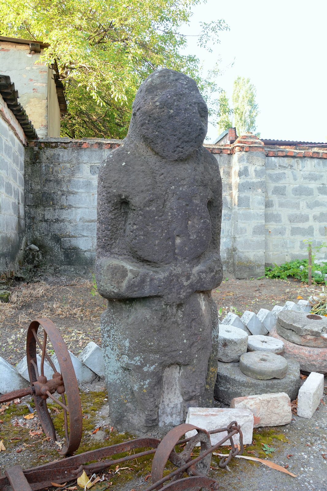 A dark stone figure of a man with his hands held at his belly, standing in a museum yard.