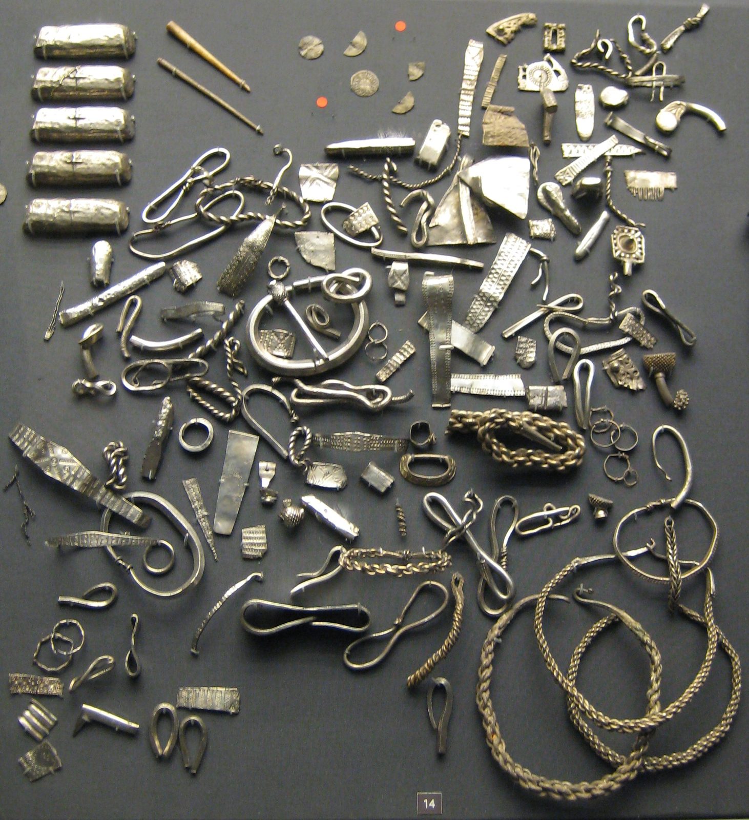 Hundreds of pieces of silver, ingots, arm-rings, chopped fragments and coins, laid out in a museum case.
