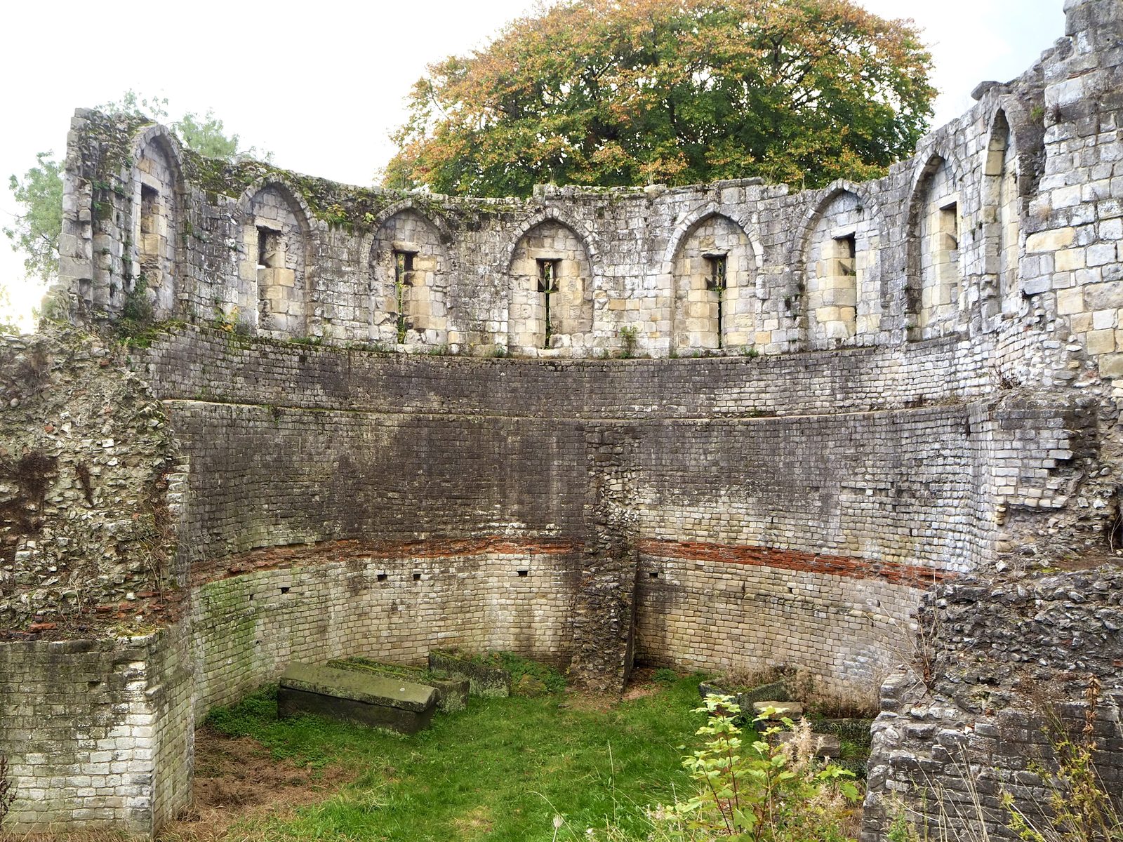 The curved inner face of a ruined stone tower, Roman masonry below and later arrow slits above.