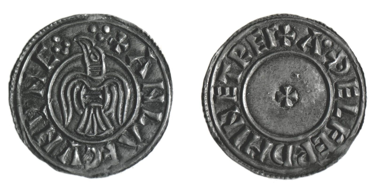 Both faces of a silver penny, a raven with spread wings on one side and a small cross on the other.
