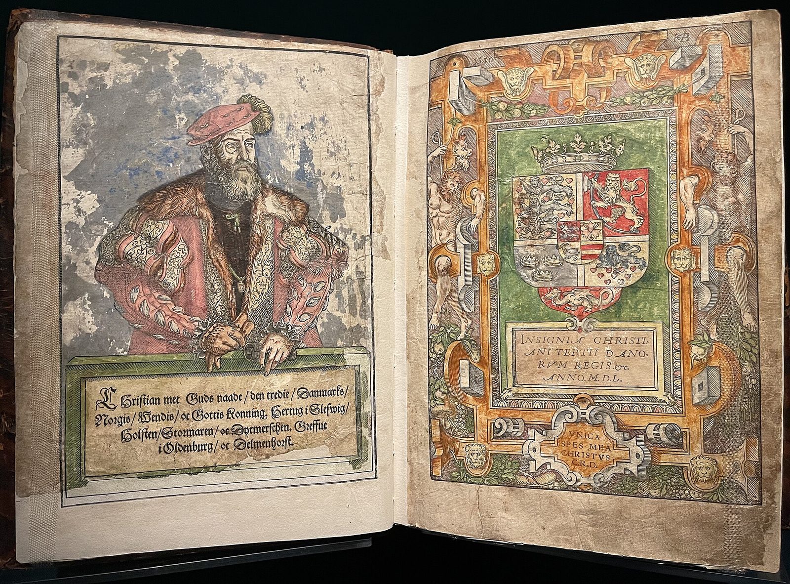 An open printed book, a hand-coloured woodcut of a bearded king on the left page and a royal coat of arms on the right.