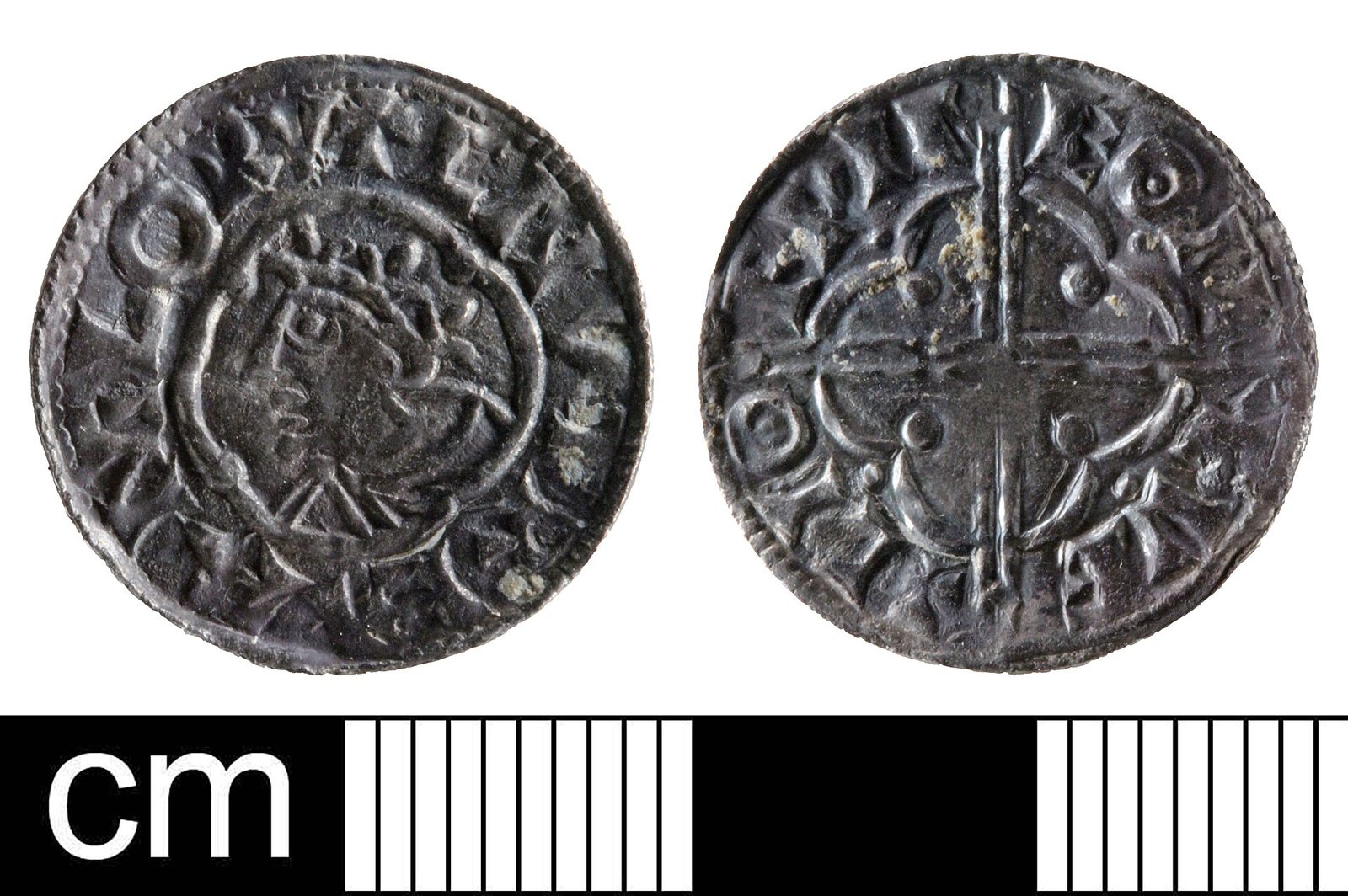 Both faces of a worn silver penny, a crowned head on one and a cross on the other, beside a centimetre scale.
