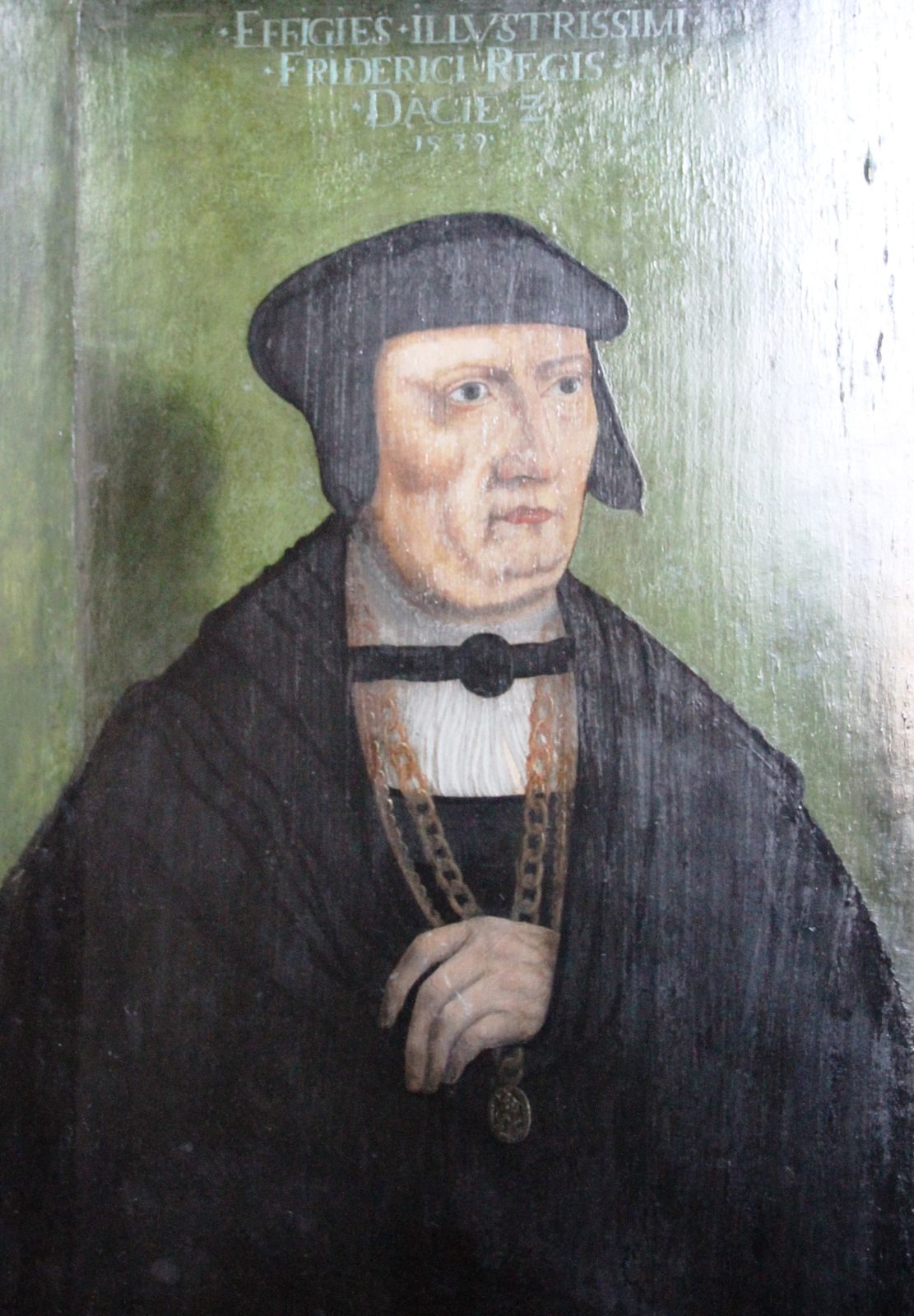 A portrait of an elderly man in a black cap and gown with a heavy gold chain, a Latin inscription above.