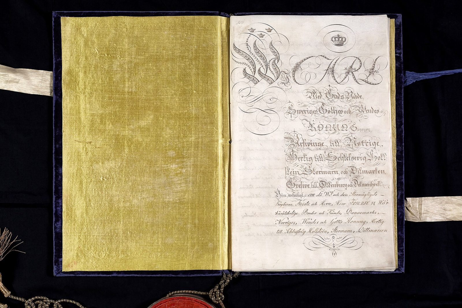 An open document in a velvet-lined case, a gold cover on the left and a handwritten title page on the right.