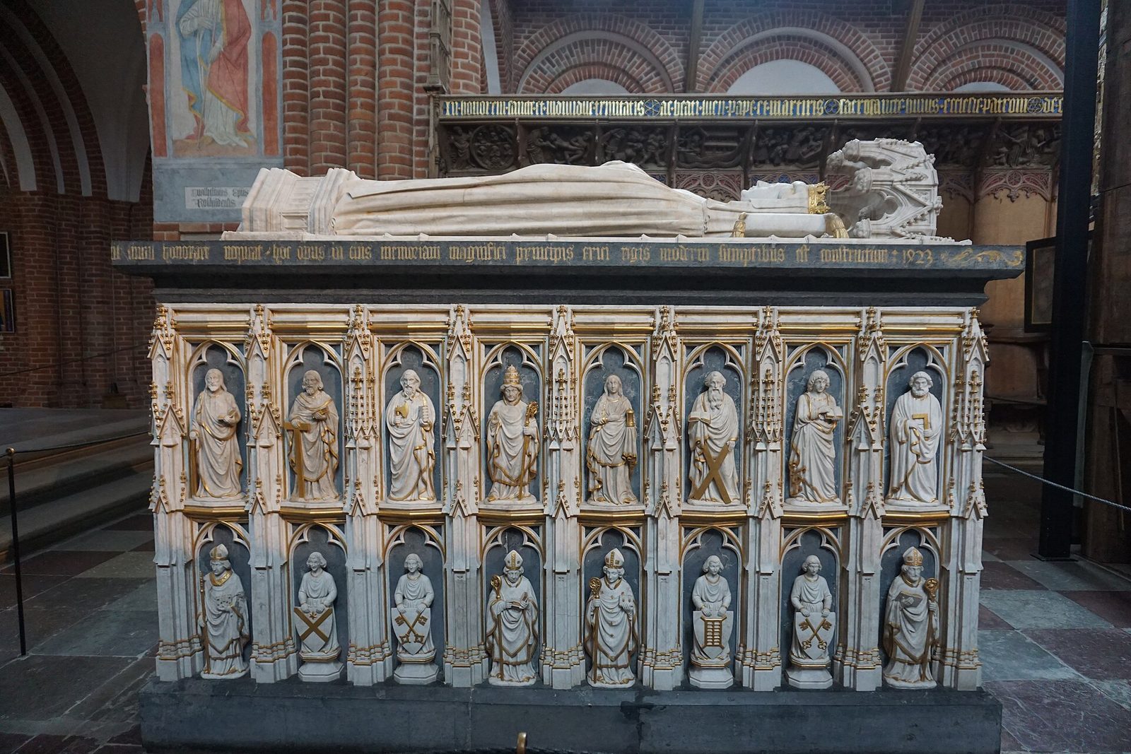 A pale stone tomb chest with rows of small carved figures in niches, a recumbent effigy lying on top.