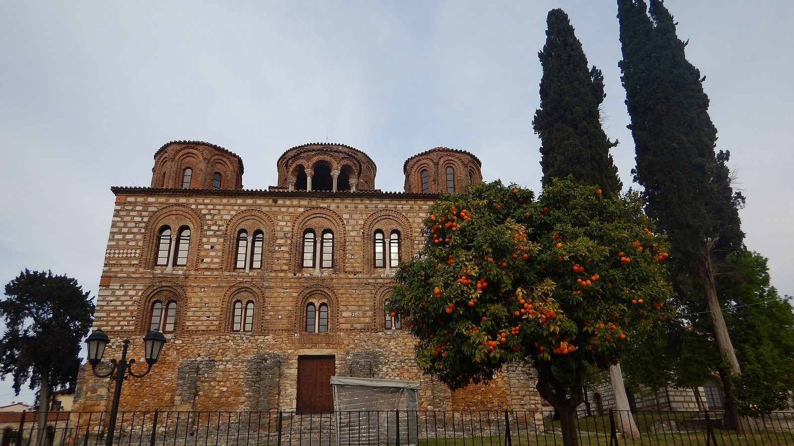 A tall square brick-and-stone church with tiers of arched windows and five domes on drums above a heavy cornice, standing in a paved enclosure.