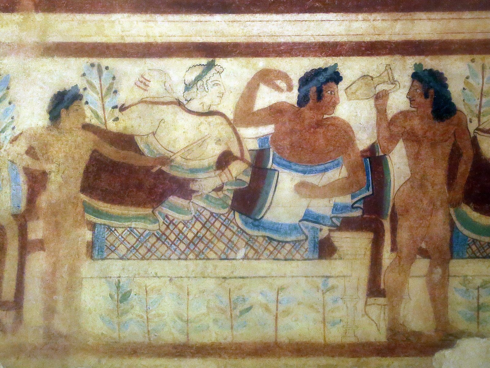 A tomb wall painting of reclining banqueters on couches, with servants and stylised trees, in red, blue and ochre.