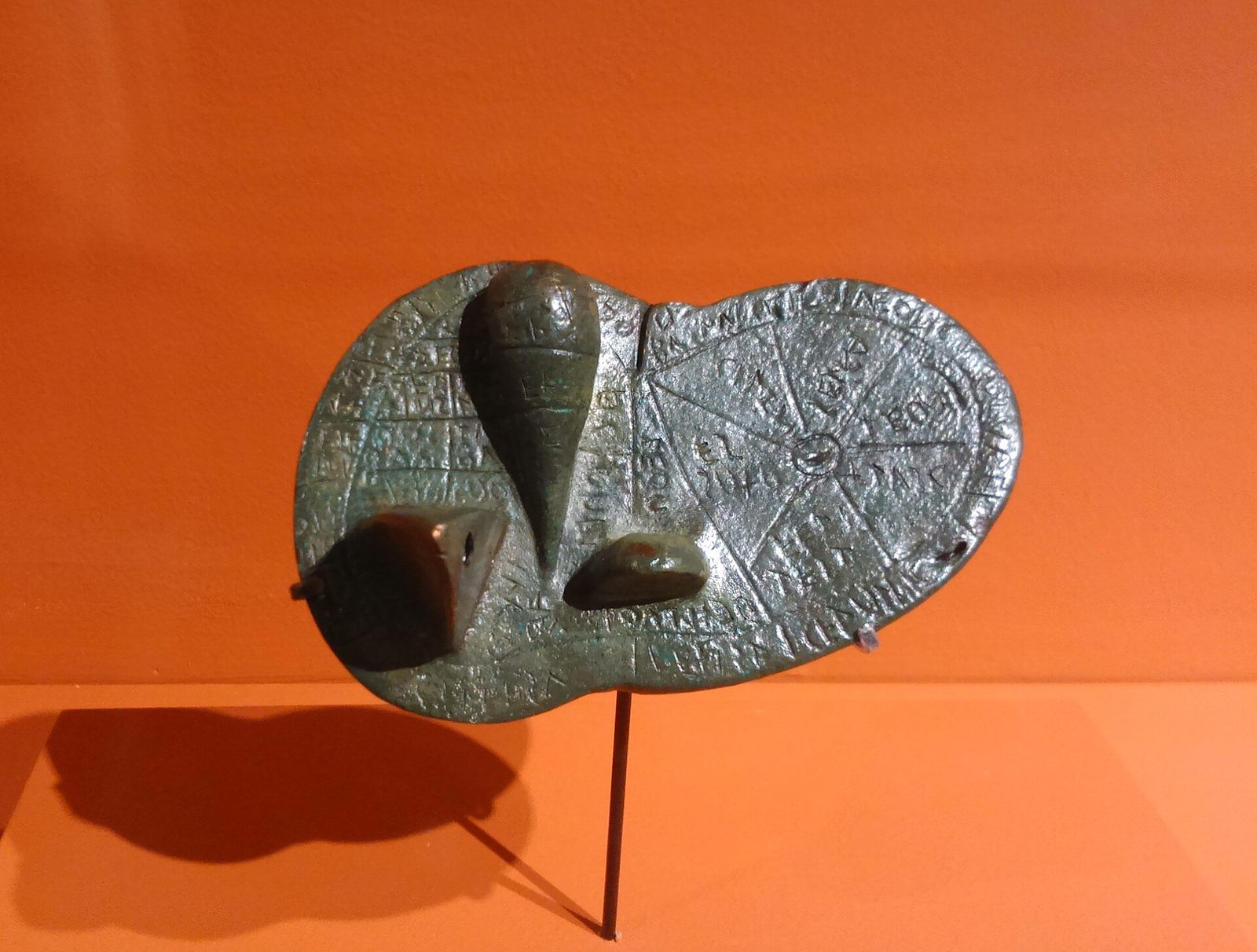 A small flat bronze model of a sheep's liver on a stand, its surface divided into inscribed compartments.