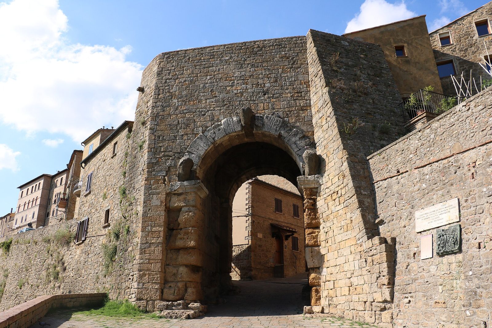 An ancient arched stone gateway in a town wall, with weathered heads set above the arch.