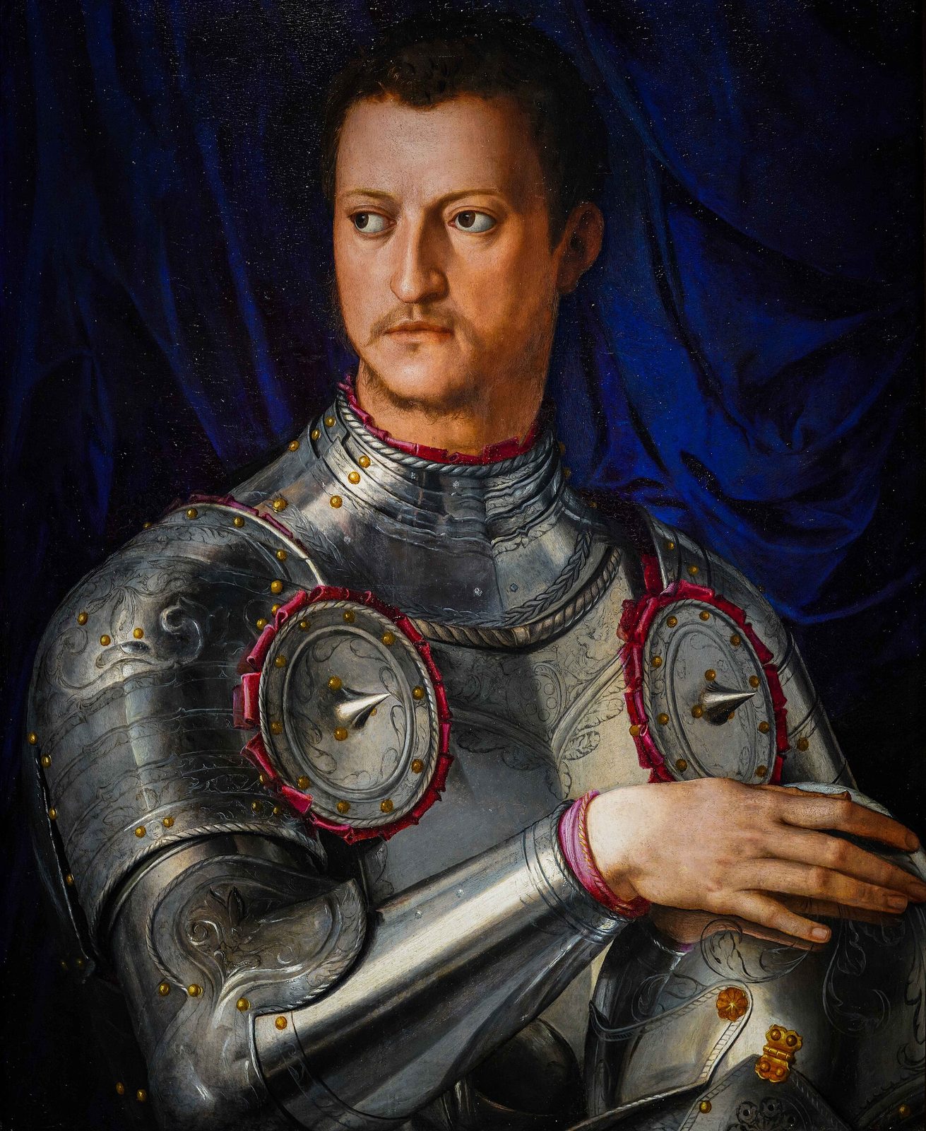 A painted half-length portrait of a young man in polished plate armour, one hand resting on a helmet, a red cloth tied at the shoulder and a dark blue curtain behind.