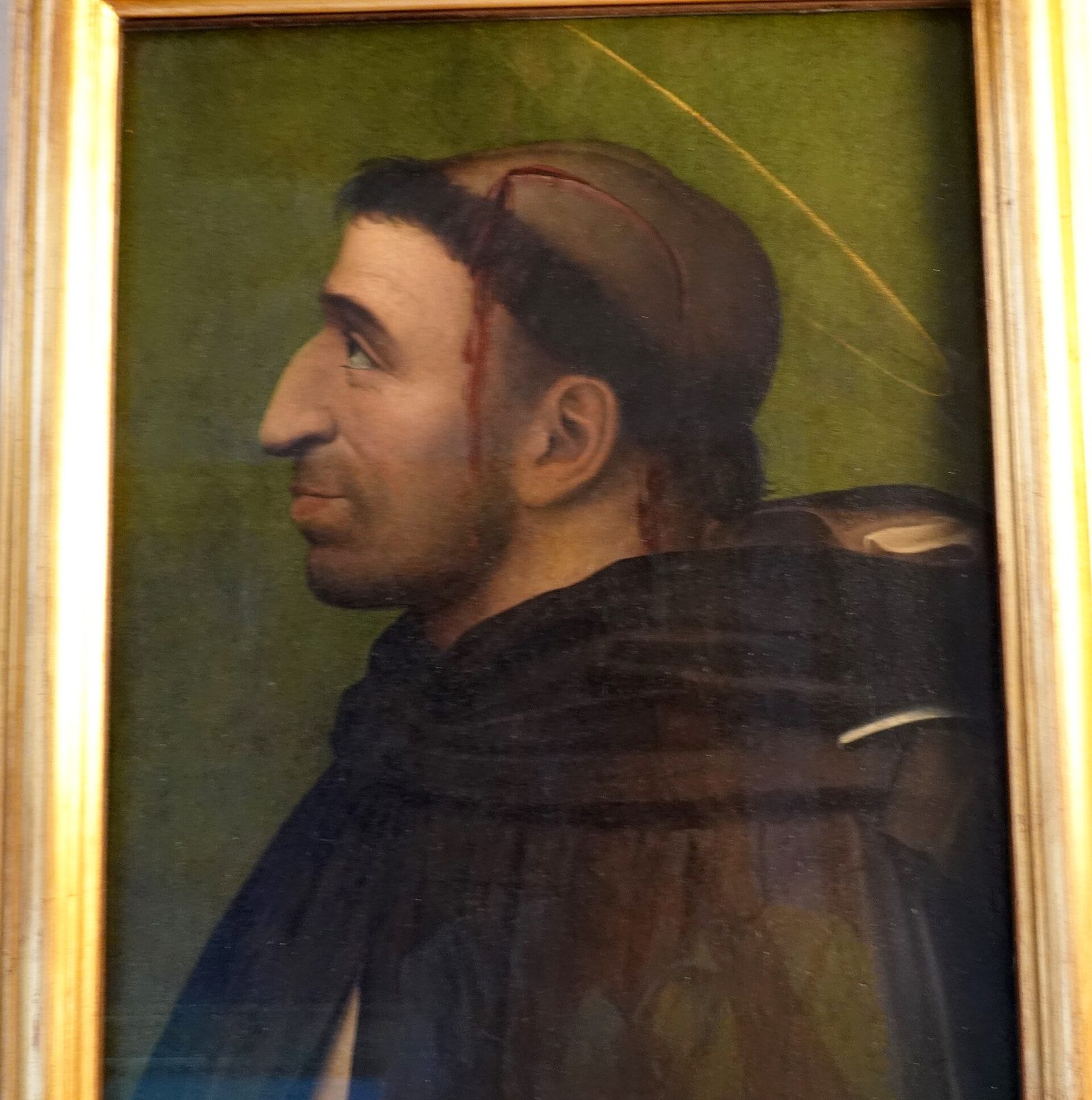 A small painted panel in a gilt frame: a man in a dark friar's habit and hood, shown in strict profile against a plain green ground, with a heavy brow and a hooked nose.