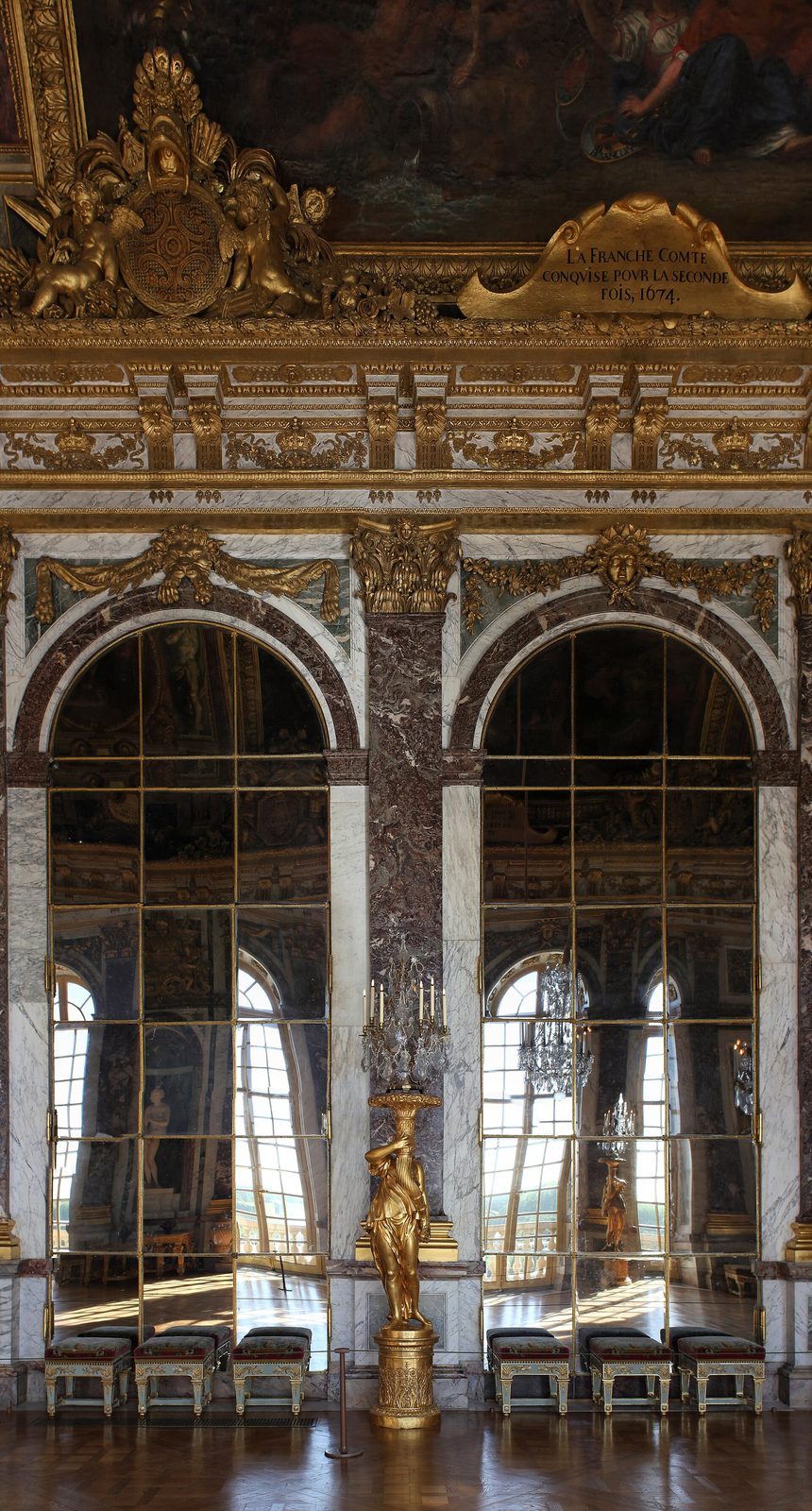 A long gallery lined on one side with tall arched mirrors and on the other with windows, a painted and gilded vaulted ceiling above and chandeliers down the length of it.