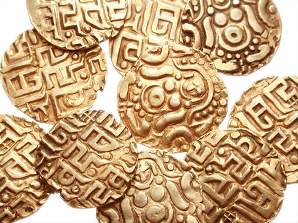 A heap of small gold coins with a seated goddess on some and Nagari script on others.