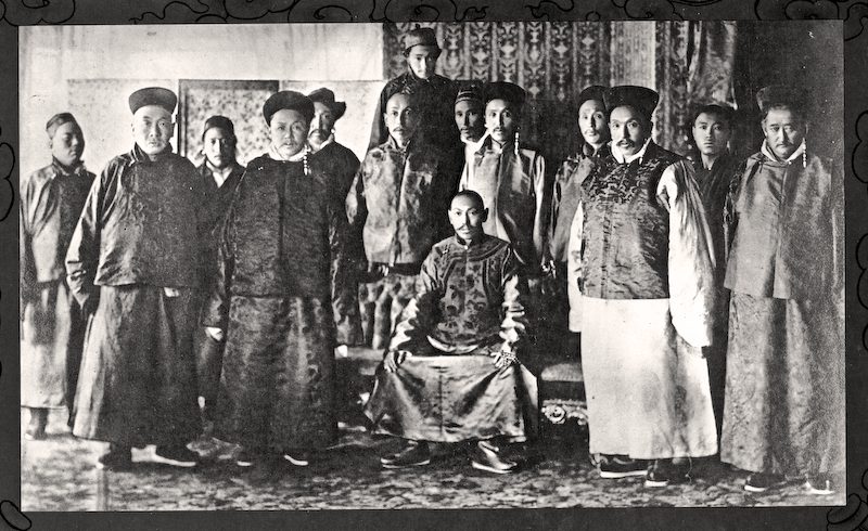 A black-and-white group photograph of men in robes and caps, one seated in the centre.